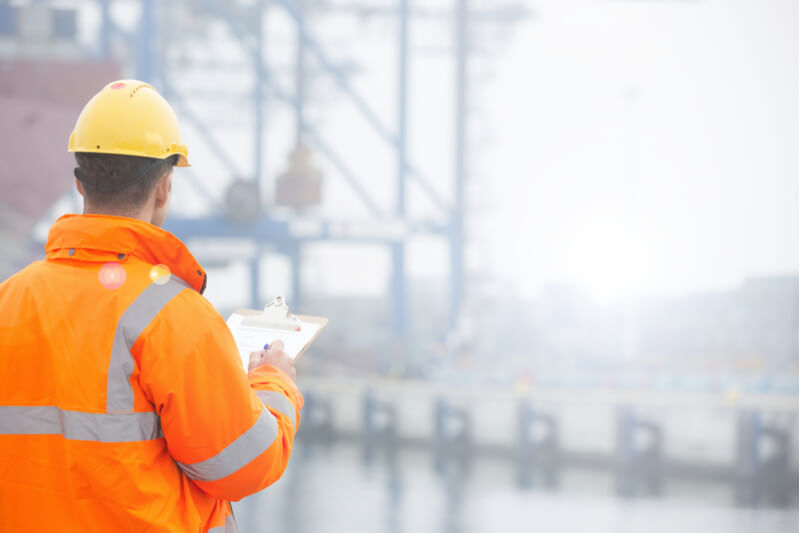 work man wearing orange hi visibility workwear in a port